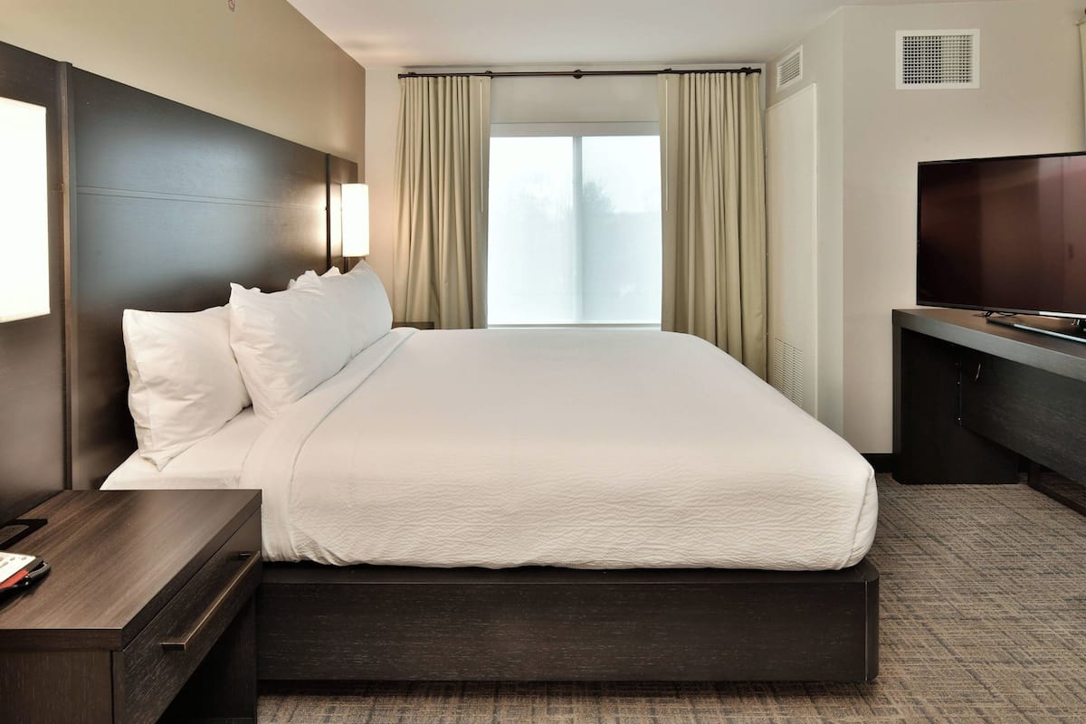 Une chambre d’hôtel avec un grand lit, une télévision, un bureau et une fenêtre avec des rideaux.