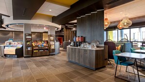 Una cafetería moderna con mostrador central, zona de estar y amplia variedad de comida y bebidas.