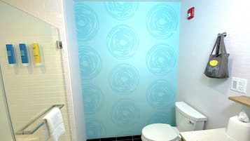 Un baño con inodoro, toallero, cabina de ducha de cristal y una pared con diseño circular.