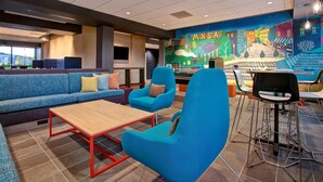 A modern lounge area with a blue sofa set, a wooden coffee table, and a mural depicting a colorful street scene. - Tru by Hilton Manassas (Manassas)