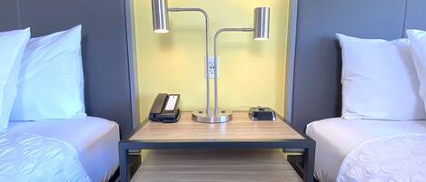 Habitación de hotel con dos camas, una mesita de noche con lámpara, teléfono y una pequeña mesa con control remoto.