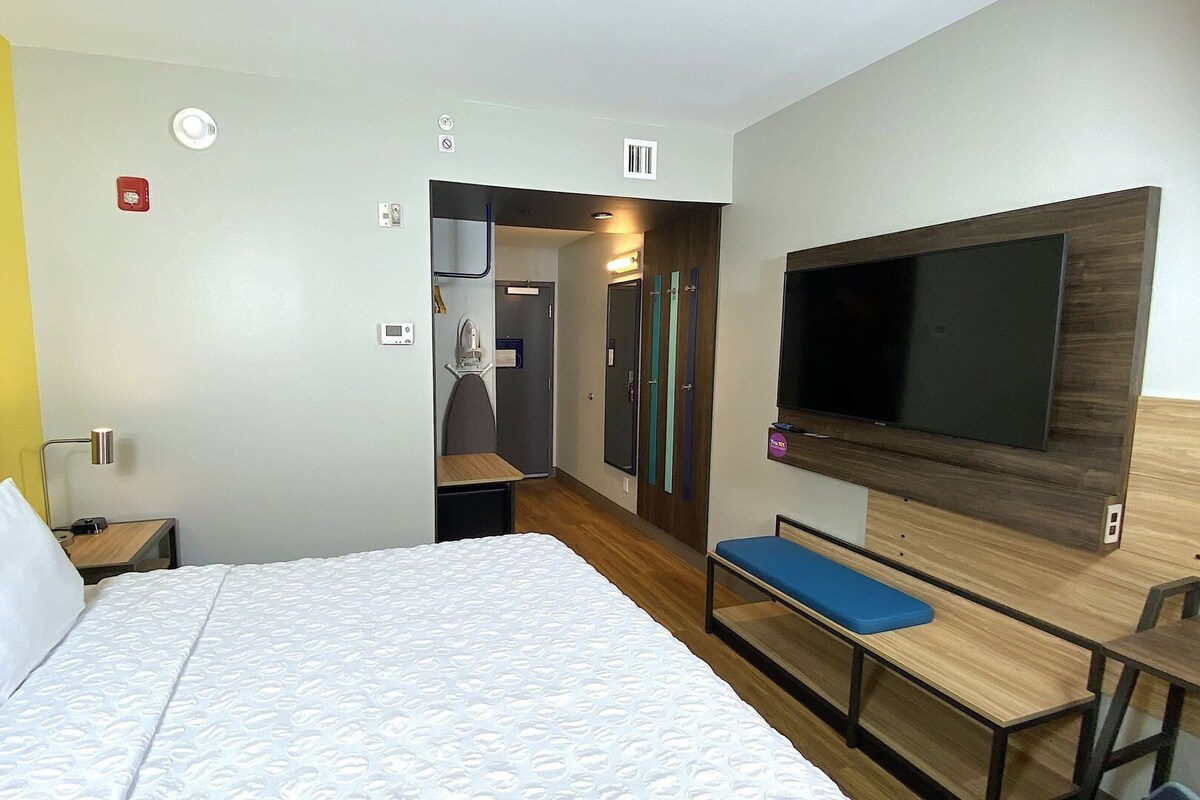 A hotel room with a bed, a desk, a TV, and a shower area.