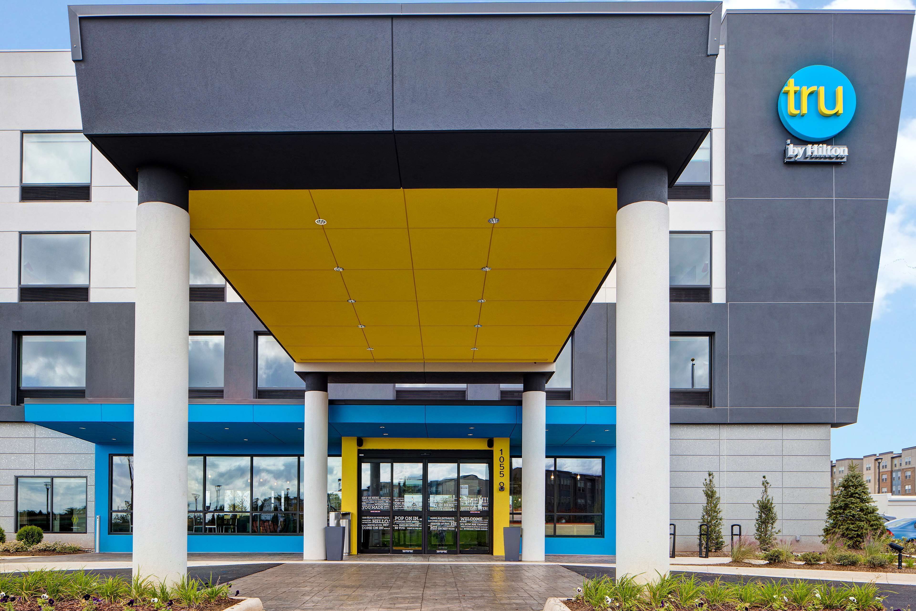 Entrada moderna de un hotel con toldo amarillo, fachada azul y gris, y el logotipo de Hilton a la vista.
