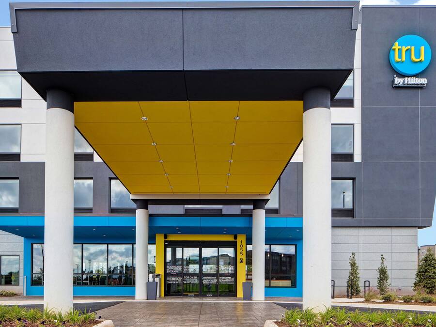 Een moderne hotelentree met een geel luifel, blauw en grijs gevel en een zichtbaar Hilton logo.