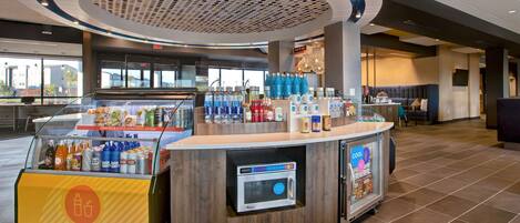 Una estación de bebidas autoservicio con microondas, diversas bebidas y aperitivos.