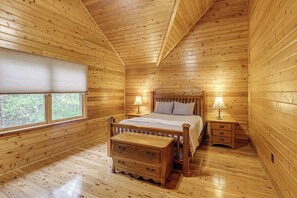 Camera da letto in una baita di legno con un letto, comodini, una cassettiera e una finestra.