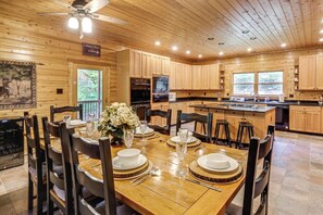 Una baita in legno con zona pranzo apparecchiata per quattro persone, con un grande tavolo di legno, sedie e una ventola a soffitto.