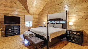 Een slaapkamer in een blokhut met een hemelbed, een televisie, een bankje en een nachtkastje.