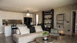 A modern living area with a sofa, armchair, and coffee table, a kitchen with white cabinets, and a dining area. - Luxe Coastal Escape with Sea Views - Kumo Villa I (Rethymno)