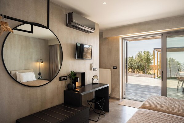 A modern hotel room with a large mirror, a flat-screen TV, a desk, and a sliding glass door leading to an outdoor area.