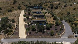 A hillside property with a modern multi-story building, a paved driveway, and surrounding vegetation. - Luxe Coastal Escape with Sea Views - Kumo Villa I (Rethymno)