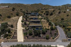 Propiedad en una ladera con un edificio moderno de varios pisos, camino pavimentado y vegetación circundante.