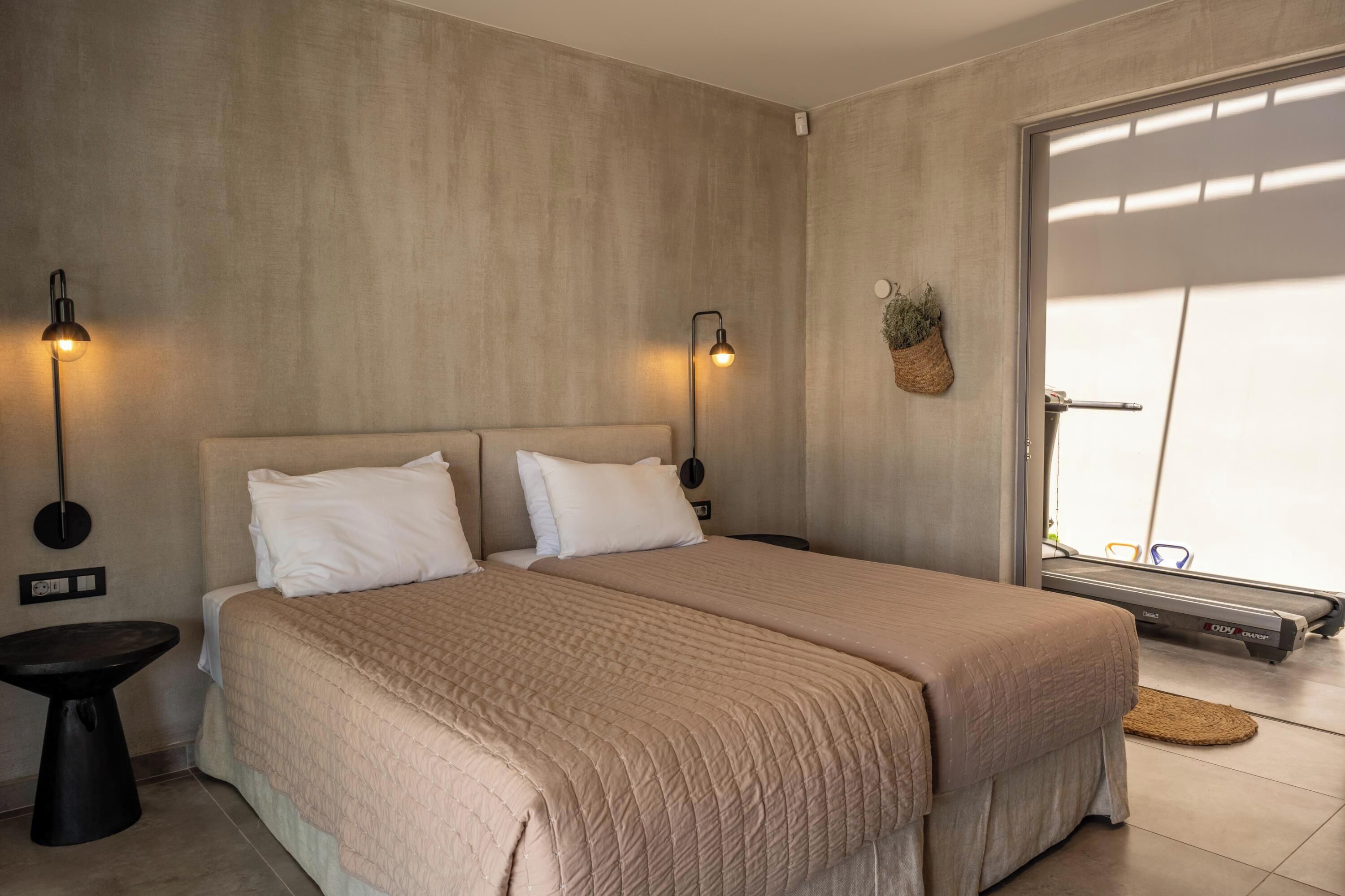 Een slaapkamer met een bed, twee wandlampen, een kleine tafel, een wandplant en een schuifdeur naar een balkon.