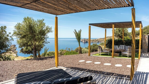 A covered outdoor seating area with a view of the sea, a lounge chair, and a pergola structure. - Luxe Coastal Escape with Sea Views - Kumo Villa I (Rethymno)