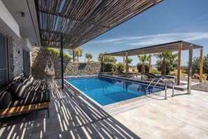 Un área de piscina con un pérgola, asientos y un muro de piedra.