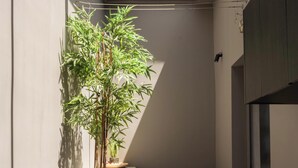 A compact kitchen with a built-in washing machine, a potted bamboo plant, a wicker chair, and a large window. - Luxe Coastal Escape with Sea Views - Kumo Villa I (Rethymno)