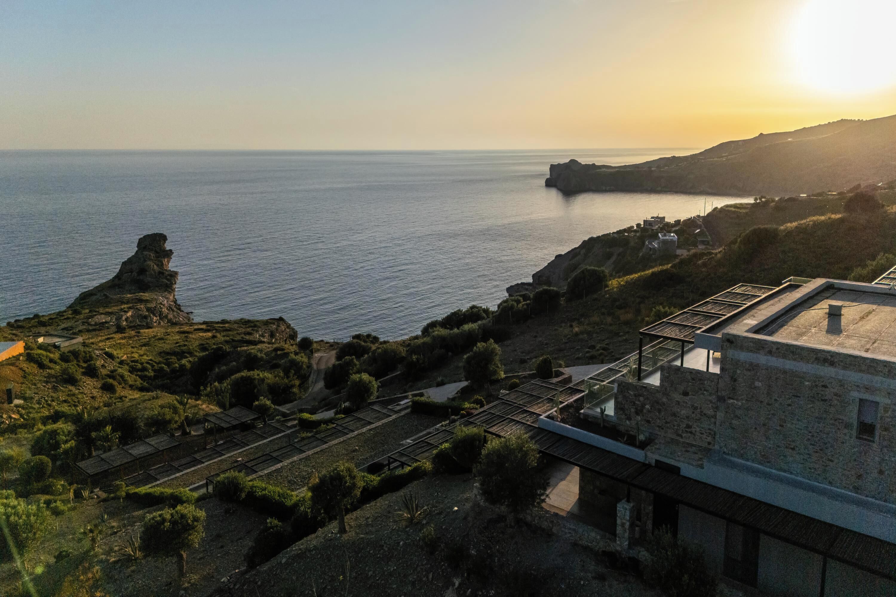 A coastal landscape with a prominent rock formation, a building with a flat roof, and a railway track.