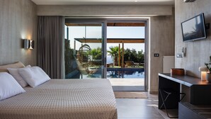 A modern hotel room with a large bed, a desk with a lamp, a TV, and a sliding glass door leading to a pool area. - Luxe Coastal Escape with Sea Views - Kumo Villa I (Rethymno)