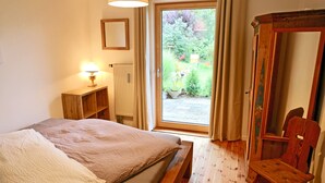 Et soveværelse med en seng, en træstol, et natbord, en lampe og udsigt til en have gennem en skydedør.