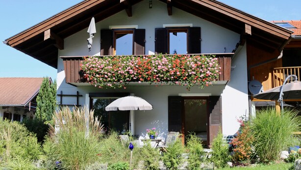 Et toetagers hus med en balkon pyntet med blomster, en hvid parasol og et spiseområde med udendørs møbler.
