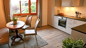 Et køkken med hvide skabe, en indbygget ovn og et spiseområde med et rundt bord og stole.