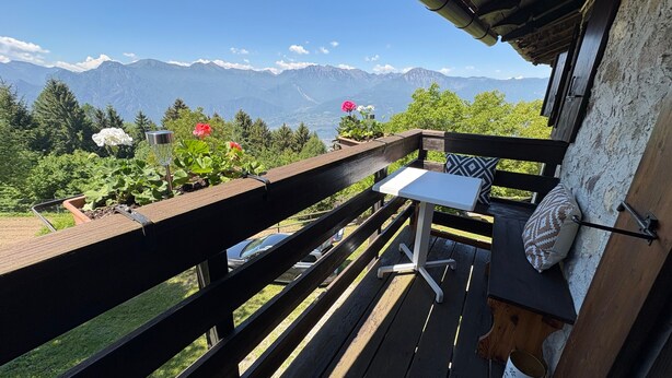 Eine Holzterrasse mit Tisch und Stühlen mit Blick auf eine gebirgige Landschaft.