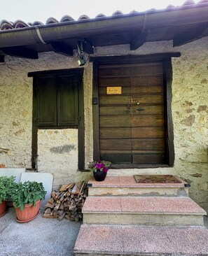 Un edificio rústico con puerta de madera, una ventana pequeña y felpudo.