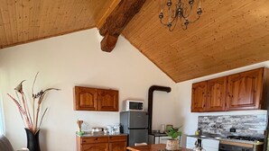 Ein gemütliches Wohnzimmer mit einer Couch, einem Esstisch mit Stühlen, Holzschränken, einer Küchenzeile mit Geräten und einer Pendelleuchte.