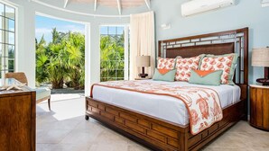 A bedroom with a large bed, a wooden headboard, a nightstand, and a window with a view of greenery. - Amazing Waterfront Villa (Providenciales)