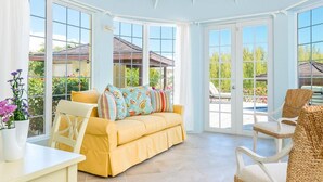 A conservatory with a yellow sofa, wicker chairs, and large windows offering views of the outdoors. - Amazing Waterfront Villa (Providenciales)