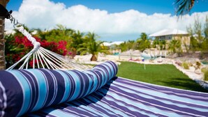 A hammock with striped cushions in a tropical setting with a pool and palm trees. - Amazing Waterfront Villa (Providenciales)