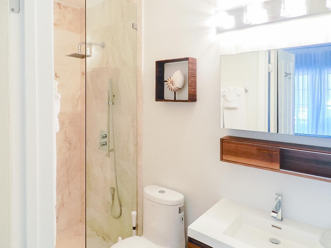 A bathroom with a glass-enclosed shower, a white sink, and a mirror with a wooden frame.