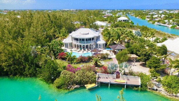 A large, circular building surrounded by lush greenery and a turquoise pool. - Amazing Waterfront Villa (Providenciales)