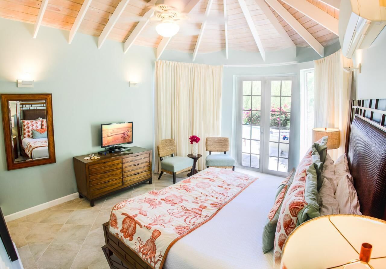 Un dormitorio con cama, cómoda, televisor y ventana con cortinas.