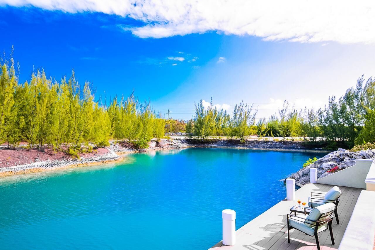 Zona junto a la piscina con vista a una piscina azul cristalina, rodeada de árboles y una terraza con mobiliario exterior.