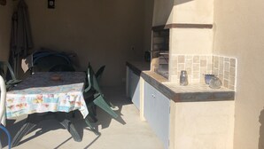 Ein kleiner Außenbereich mit Kochgelegenheit, einem Tisch und Stühlen, einer gefliesten Rückwand und einer Holzbeschichtung an der Decke.