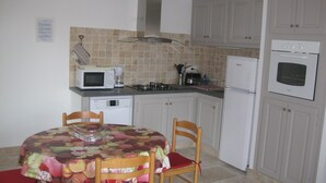 Eine kompakte Küche mit Mikrowelle, Herd und Backofen, einem Esstisch mit Stühlen sowie einer gefliesten Spritzschutzwand.