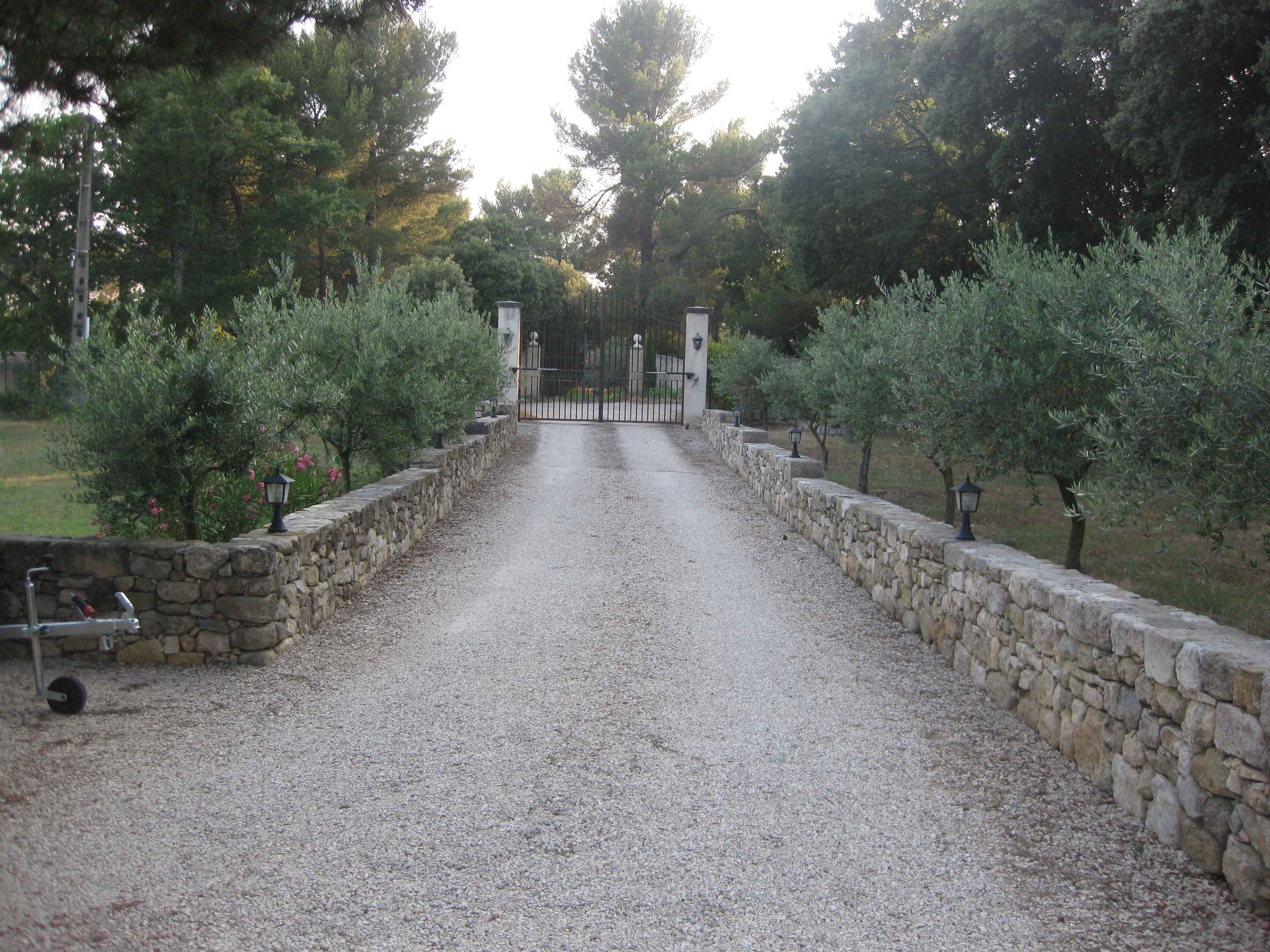 A gravel driveway leading to a gated entrance surrounded by stone walls and trees.