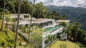 Una casa moderna de varios pisos con piscina, rodeada de exuberante vegetación y colinas.