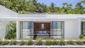 Una habitación de hotel moderna con una cama grande, un baño con bañera y vistas a vegetación exuberante.