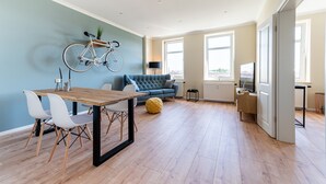 Una sala de estar moderna con una mesa de comedor de madera, sillas blancas, un sofá azul y una bicicleta colgada en la pared.