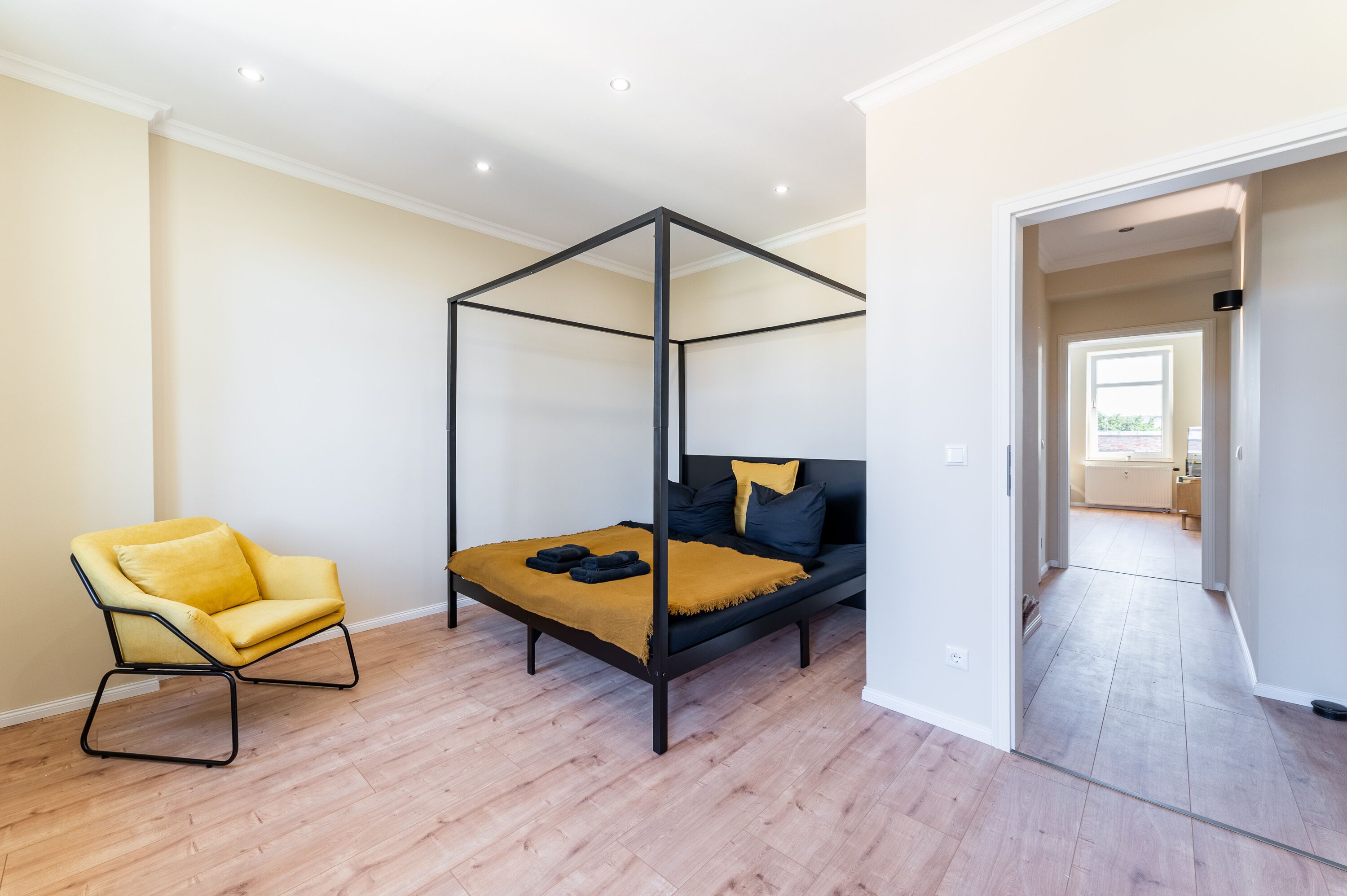 A bedroom with a four-poster bed, a yellow armchair, and a wooden floor.