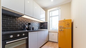 Una cocina con estufa negra, armarios blancos, salpicadero de ladrillo y refrigerador amarillo.
