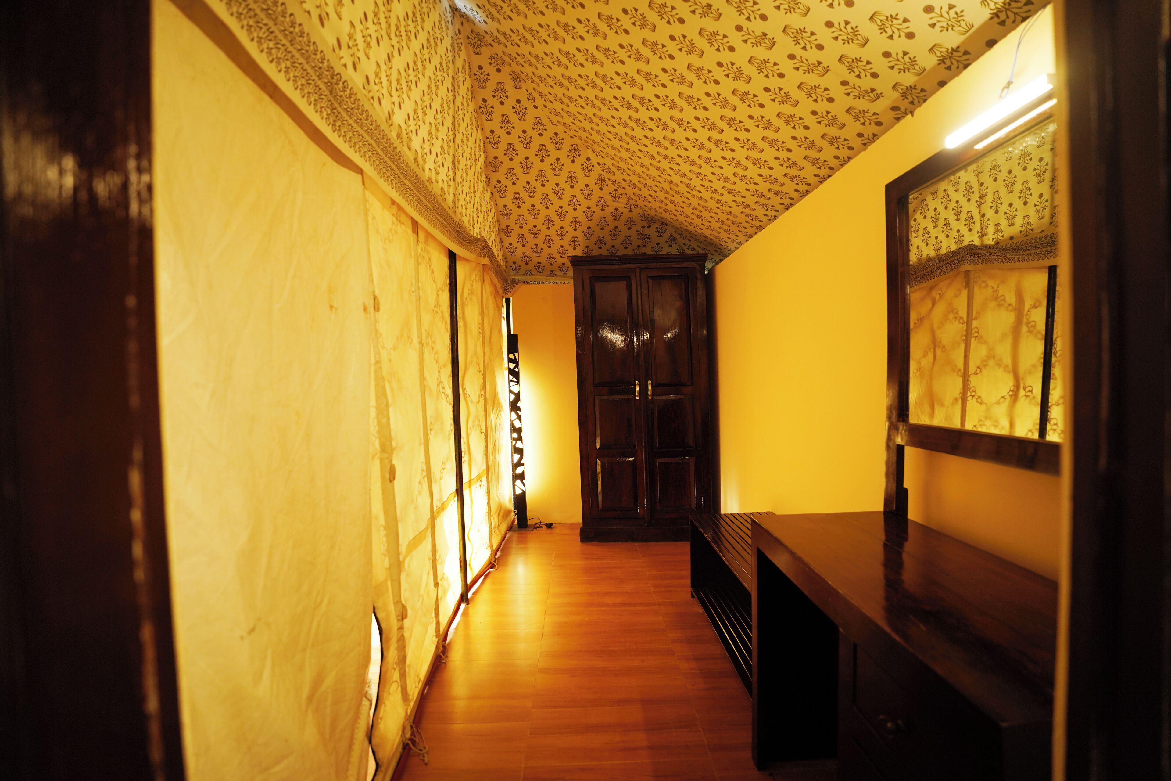 A narrow hallway with patterned wallpaper, wooden flooring, and a dark wooden bench.