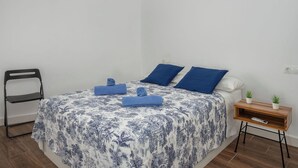 Ein Schlafzimmer mit einem Bett, einem Sessel, einem Nachttisch mit Pflanze und einer Klimaanlage an der Wand.
