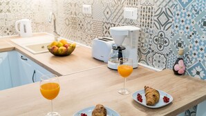 Una encimera de cocina con un frutero, tostadora, cafetera y alimentos para el desayuno, como cruasanes y jugo de naranja.