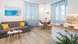 Una sala de estar moderna con un sofá gris, una mesita blanca pequeña y un comedor con una mesa y sillas de madera.