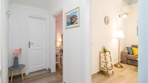 Un pasillo con una puerta blanca, una pequeña mesa con un jarrón, un cuadro en la pared, una lámpara y un sofá con cojines.