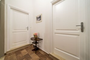 A hallway with two white doors, a small table with a vase, and a framed picture on the wall.