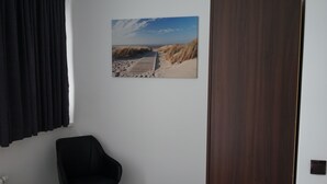 A room with a wooden door, a black chair, and a beach scene painting on the wall. - Stadtpension Heilbronn (Heilbronn)